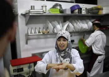 A hearing impaired employee uses sign language to communicate with a co-worker in the kitchen of a restaurant in Gaza