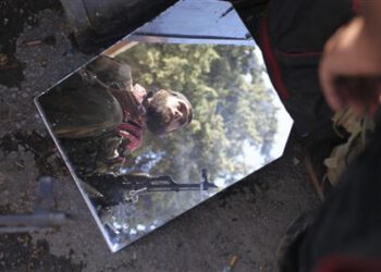 A member of the Free Syrian Army is reflected in a mirror in a house they use as a base in Haram town, Idlib Governorate