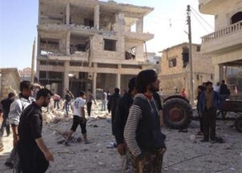 Residents walk on rubble near buildings which are damaged after a Syrian Air Force fighter jet loyal to Syria's President Bashar al-Assad fired missiles at Binsh