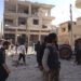 Residents walk on rubble near buildings which are damaged after a Syrian Air Force fighter jet loyal to Syria's President Bashar al-Assad fired missiles at Binsh