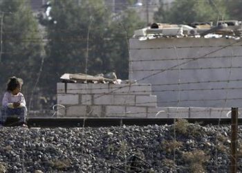 Girl sits on a railway track as she looks to cross the border fence from the northern Syrian town of Ras al-Ain into Turkey, as seen from the Turkish border town of Ceylanpinar