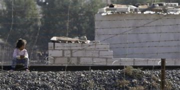 Girl sits on a railway track as she looks to cross the border fence from the northern Syrian town of Ras al-Ain into Turkey, as seen from the Turkish border town of Ceylanpinar