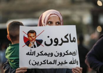 An Arab-Israeli, Muslim demonstrator, holding a child and clad in a mask due to the COVID-19 pandemic, holds up a sign during a rally protesting against French President Emmanuel Macron's anti-Islam remarks, in the Arab town of Umm-Al Fahm, Haifa district, northern Israel, Oct. 25, 2020. (AFP Photo)
