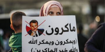 An Arab-Israeli, Muslim demonstrator, holding a child and clad in a mask due to the COVID-19 pandemic, holds up a sign during a rally protesting against French President Emmanuel Macron's anti-Islam remarks, in the Arab town of Umm-Al Fahm, Haifa district, northern Israel, Oct. 25, 2020. (AFP Photo)